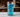 Ultra-detailed macro view of a tall glass containing nugget ice and electric blue liquid, positioned on a real surface with environmental context. The entire beverage system photographed as a unified physical object in real-world conditions.