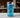 Ultra-detailed macro view of a tall glass containing nugget ice and electric blue liquid, positioned on a real surface with environmental context. The entire beverage system photographed as a unified physical object in real-world conditions.