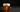 A single lowball glass holding dark amber reposado and Benedictine, crowned with a thick heavy egg white foam, tiny edible flowers resting on the surface, a large clear sculptural ice cube as the centerpiece glowing from within the liquid