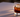 A single, crystal-clear 2.5-inch ice sphere resting in a heavy-bottomed crystal glass. The glass contains a deep, mahogany-toned liquid (Cold Brew) with visible density layers—darker at the base, slightly lighter near the surface where it meets the ice.